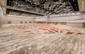 A spacious indoor area with a patterned carpet, a high ceiling with hanging lights, and a row of doors along the wall.