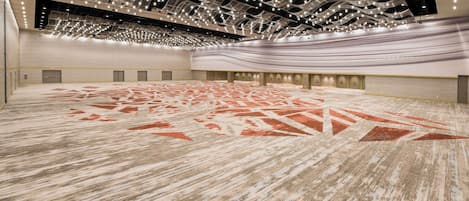 A spacious indoor area with a patterned carpet, a high ceiling with hanging lights, and a series of doors along the walls.