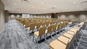 A conference room with rows of chairs, a projector screen, and a carpeted floor.