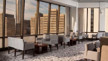 A modern hotel lobby with a city view, seating area, and a patterned carpet.