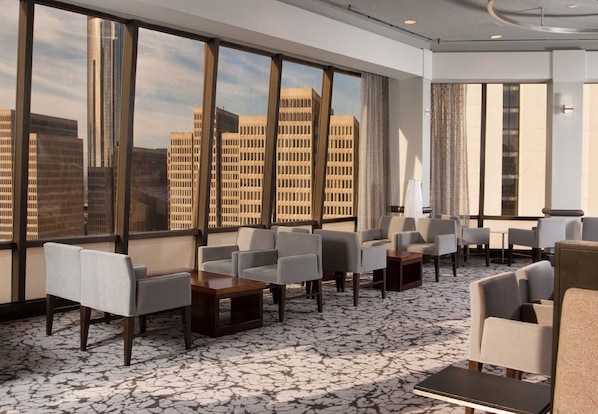 Um saguão moderno de hotel com vista para a cidade, área de estar e um tapete estampado.