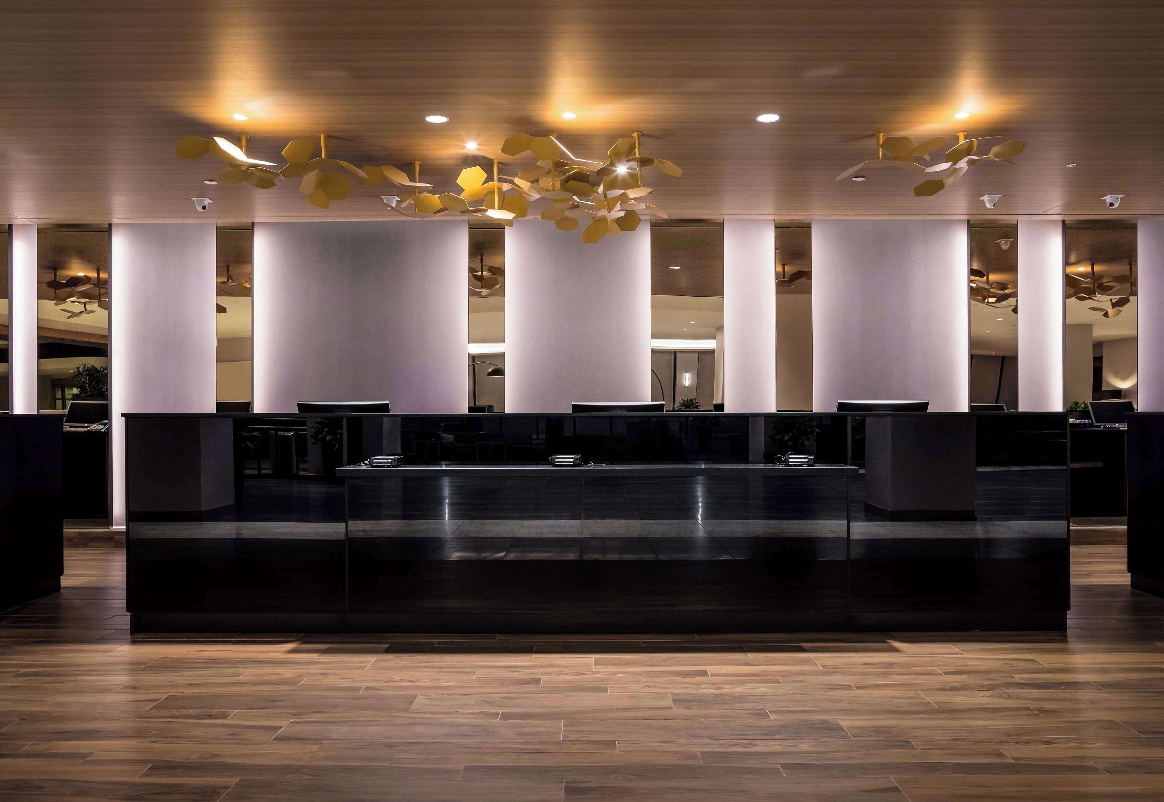 Zona de recepción con diseño moderno, que incluye un mostrador central, varias columnas e iluminación geométrica en el techo.
