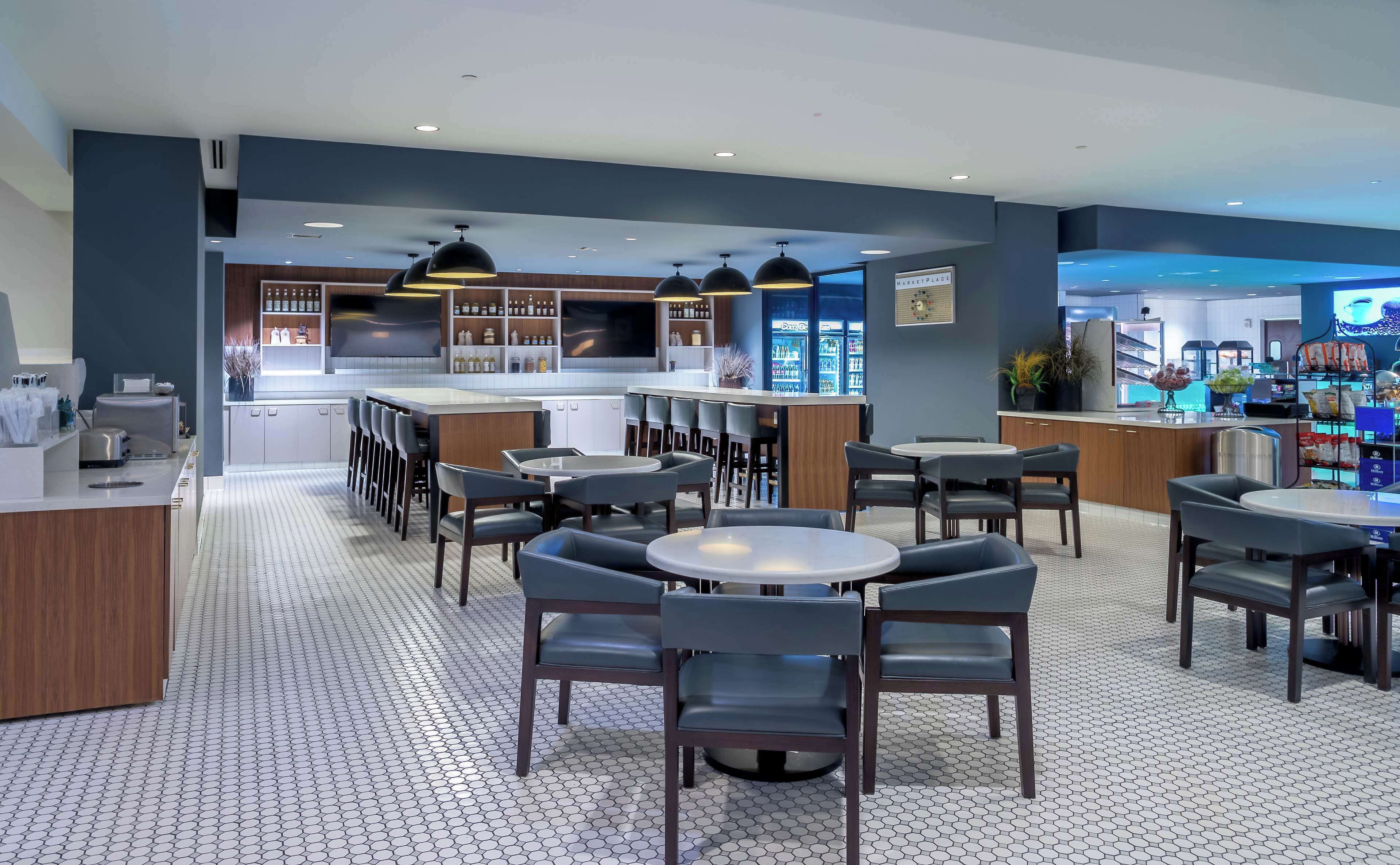 Een modern restaurant met een bar, zitplaatsen en een keuken op de achtergrond.