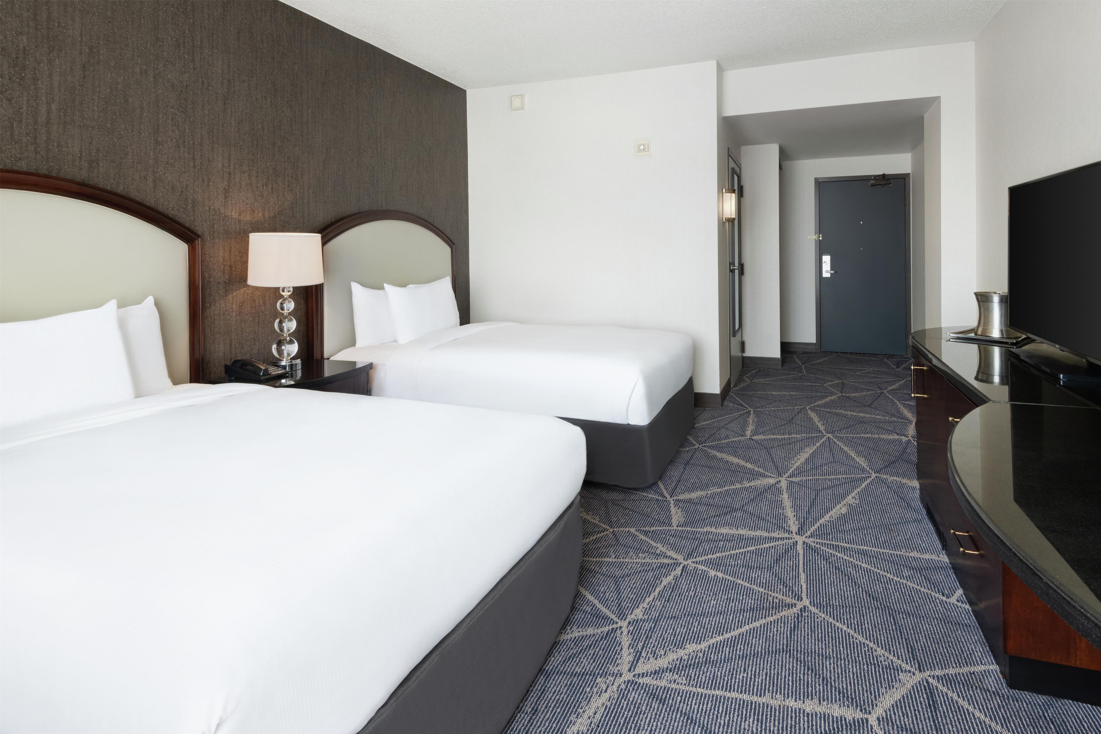 Habitación de hotel con dos camas, un escritorio, un televisor y una alfombra estampada.