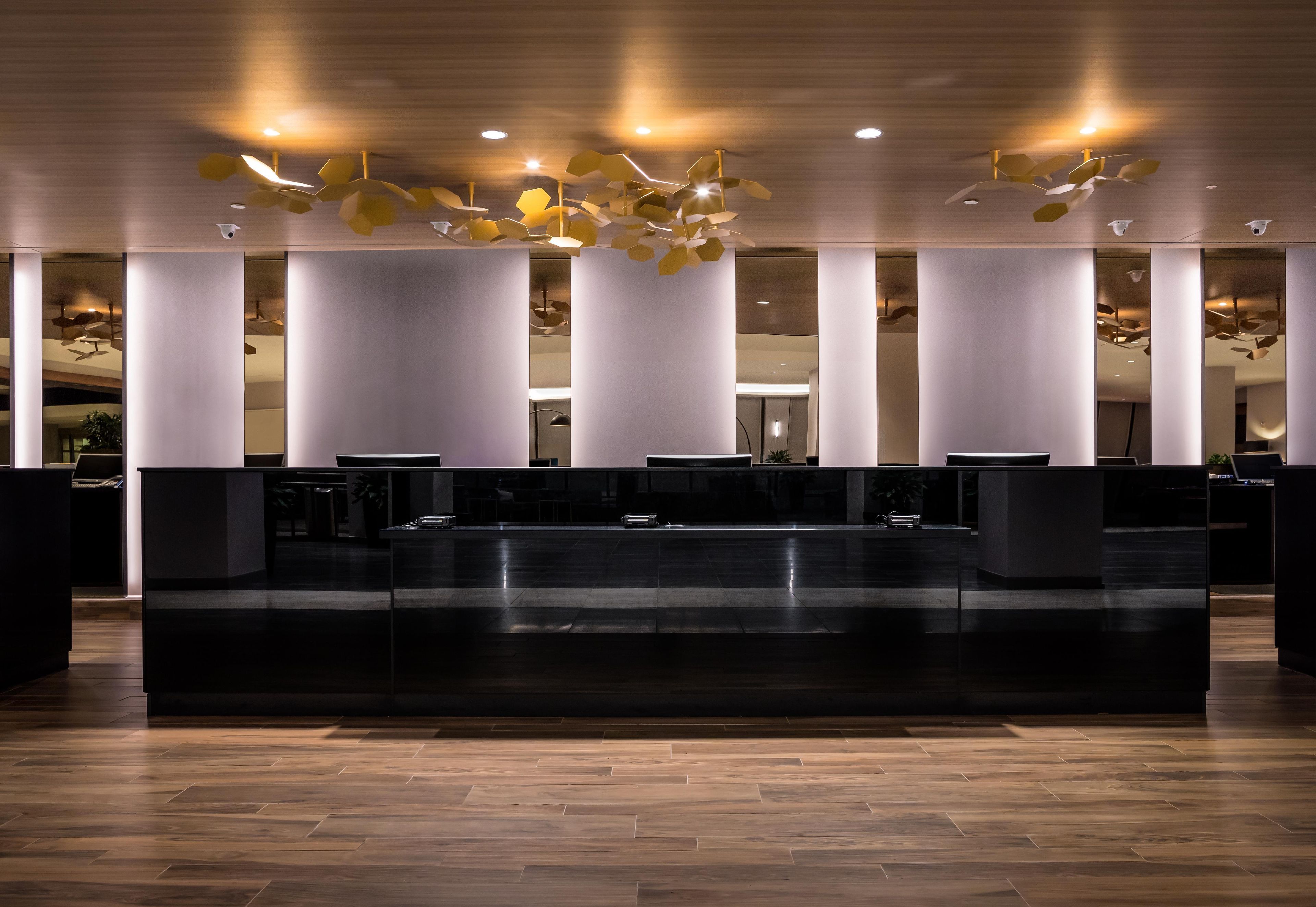Uma área de recepção com design moderno, destacando um balcão central, diversas opções de assento e um teto com luminárias geométricas.
