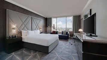 A hotel room with a large bed, a TV, a desk, and a view of the city.