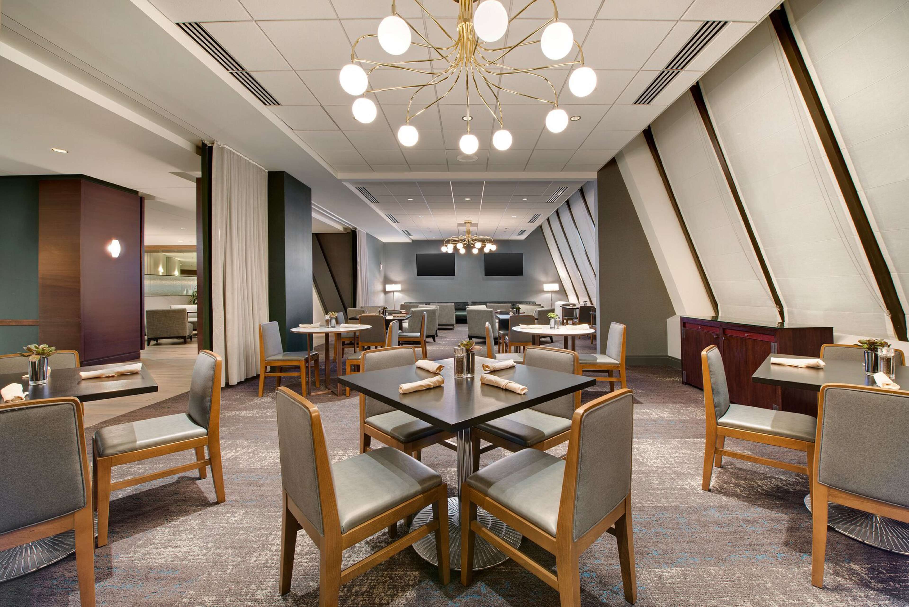 A modern hotel conference room with a large table, multiple chairs, and a chandelier.