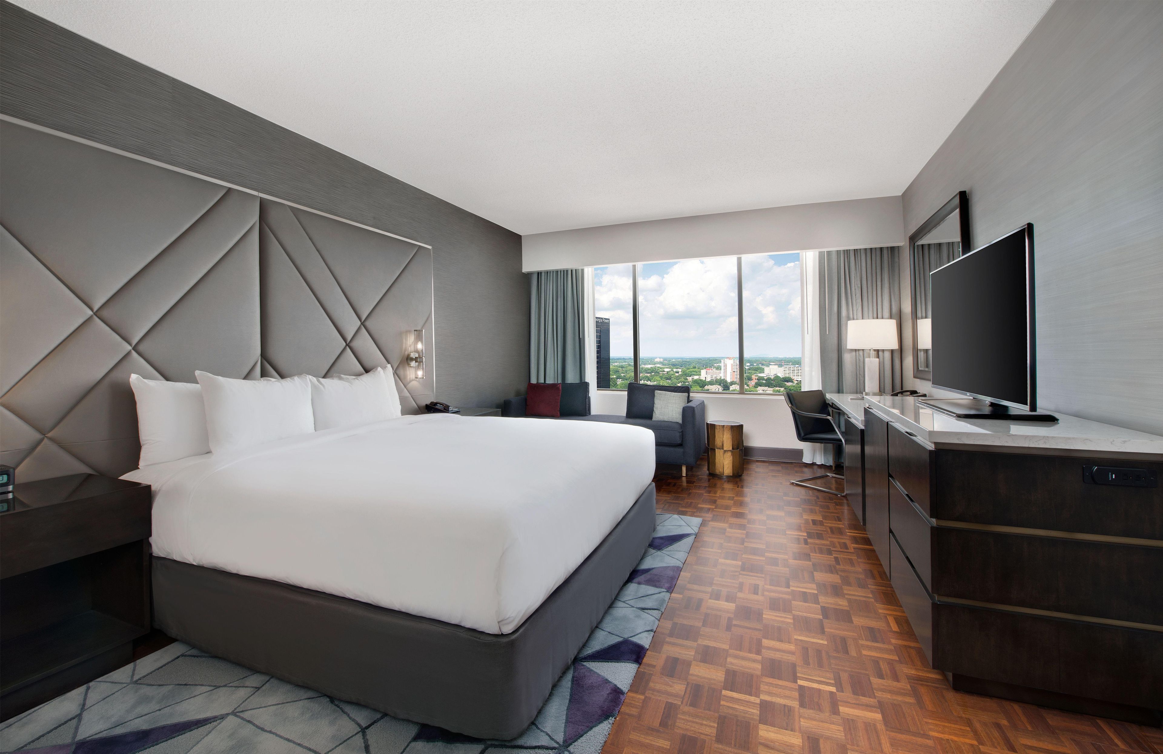 Una habitación de hotel moderna con una cama grande, un escritorio, un televisor y vistas a la ciudad.