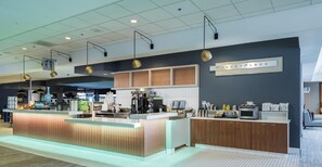 A modern coffee shop interior with a counter, espresso machines, and a sign indicating a market place. - Hilton Atlanta (Atlanta)