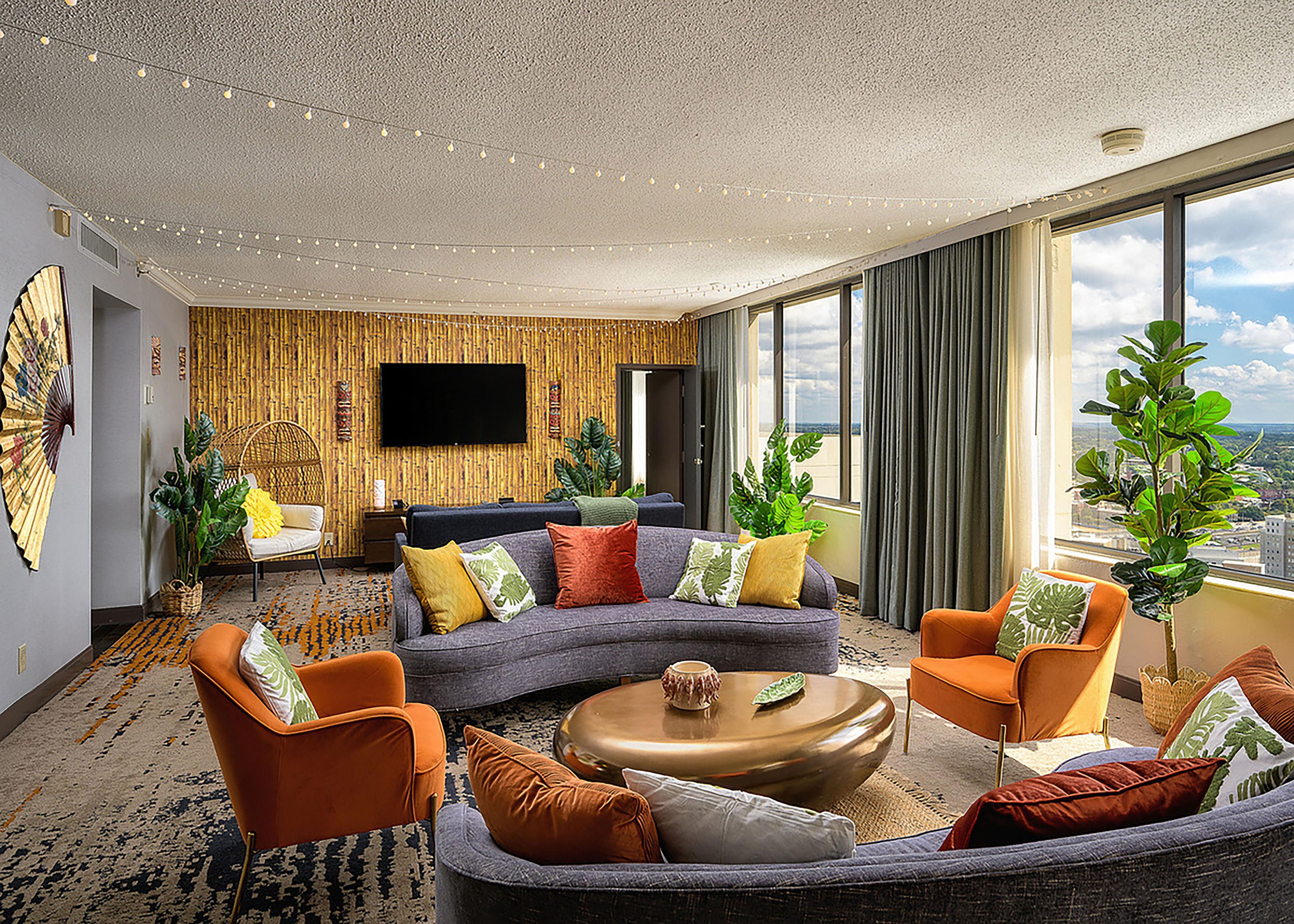 A modern living room with a sectional sofa, armchairs, a coffee table, and a flat-screen TV mounted on the wall.