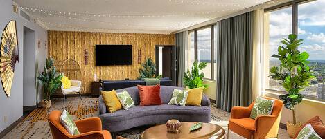 A modern living room with a sectional sofa, armchairs, a coffee table, and a flat-screen TV mounted on the wall.