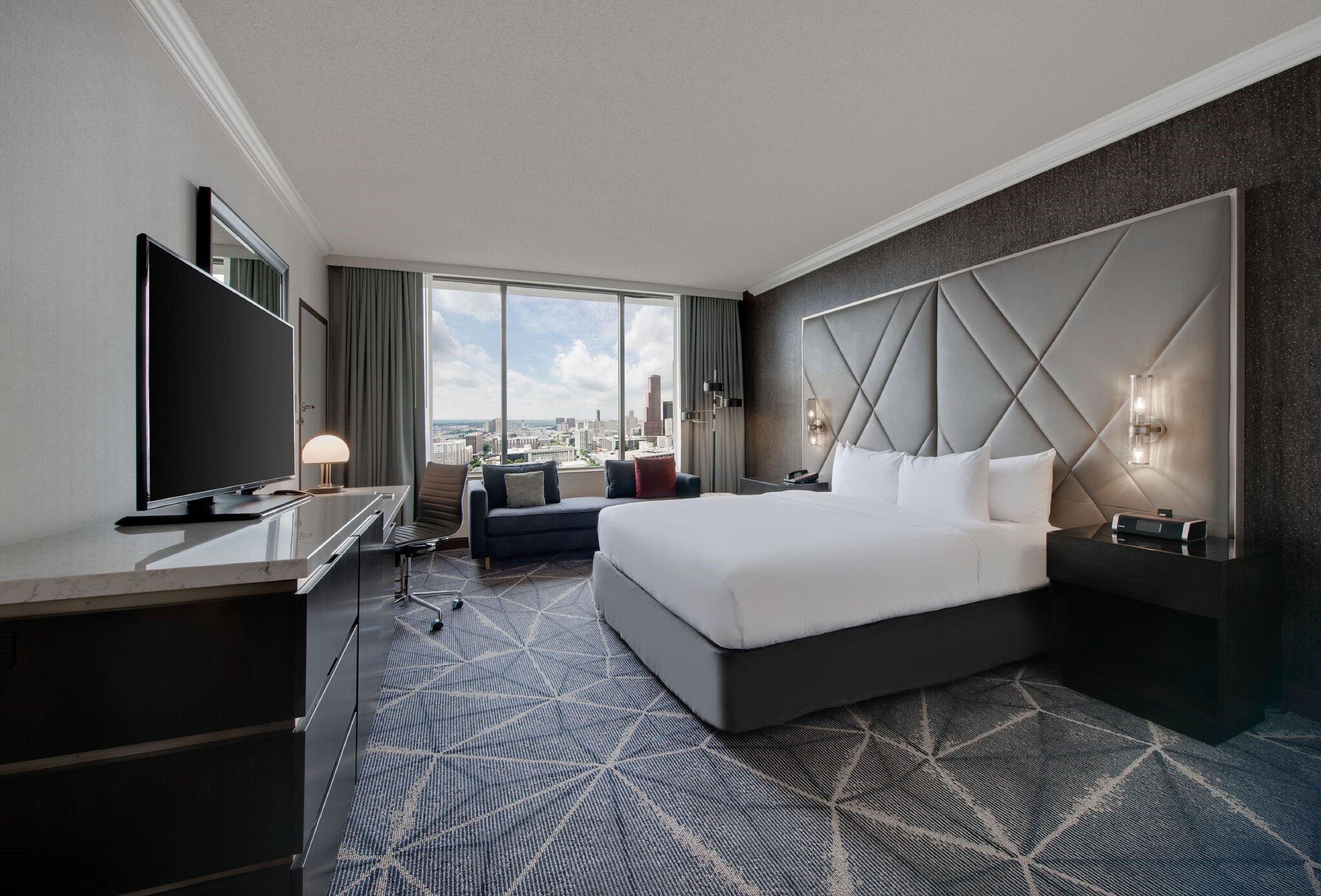 Une chambre d’hôtel avec un grand lit, un bureau doté d’une télévision à écran plat, un canapé et une vue sur la ville.