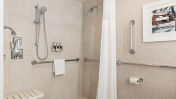 A modern bathroom with a shower, toilet, and a handrail.