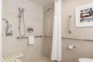 A modern bathroom with a shower, toilet, and a handrail.