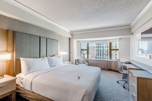 A hotel room with a large bed, a desk, and a view of the city through the window.