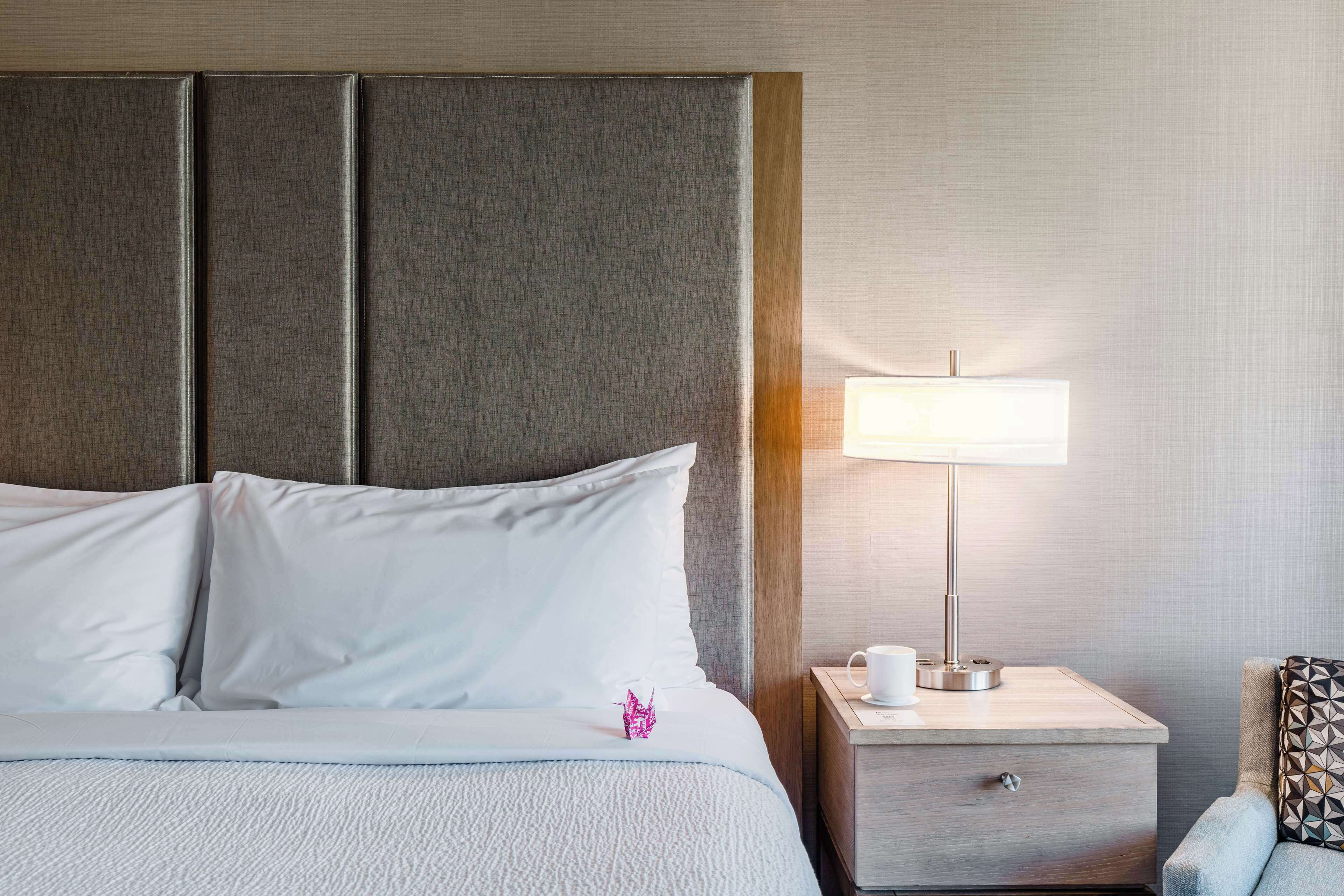 A neatly made bed with white linens, a bedside lamp, and a small decorative item on the pillow.