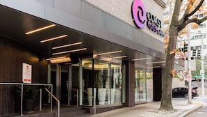 The exterior of the Coast Hotels & Apartments building with a modern design, featuring a prominent logo, a staircase leading to the entrance, and a tree with autumn leaves nearby. - Coast Seattle Downtown Hotel by APA (Seattle)