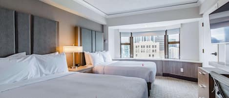 A hotel room with two beds, a large window with a city view, a flat-screen TV, and a minibar.