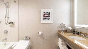 Un baño moderno con inodoro, bidé y ducha. Hay un cuadro en la pared y un lavabo con artículos de aseo.