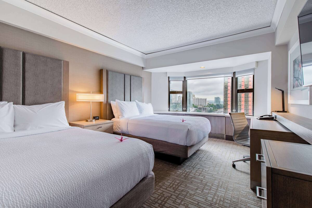 A hotel room with two beds, a desk, and a chair.