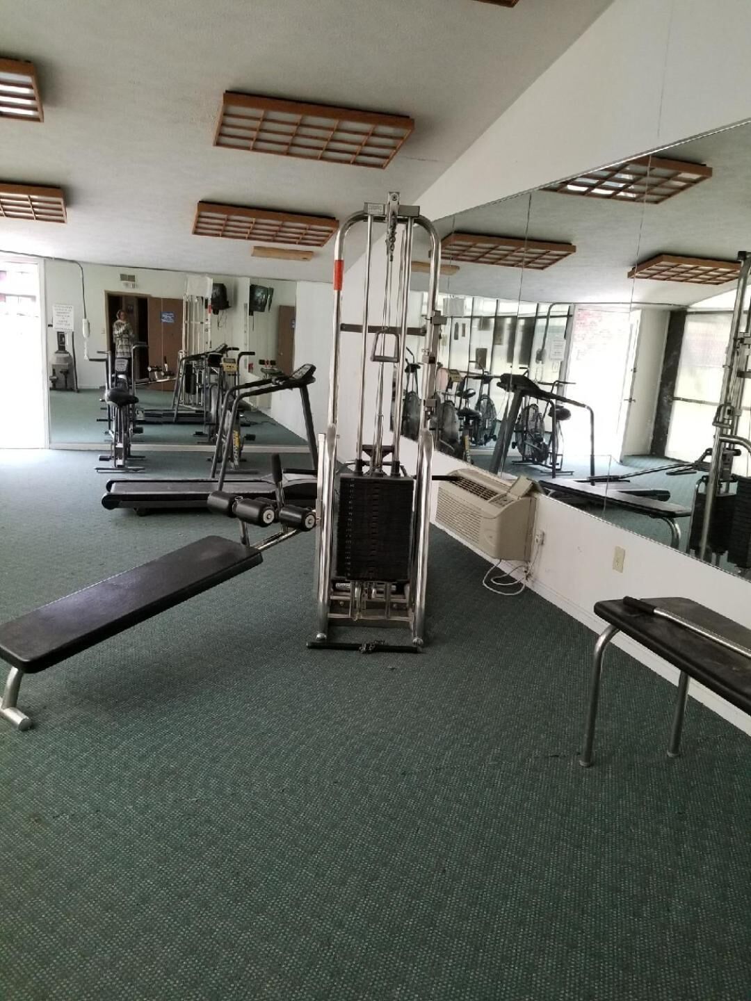 Een sportschool met trainingsapparatuur, spiegels en een bankje.