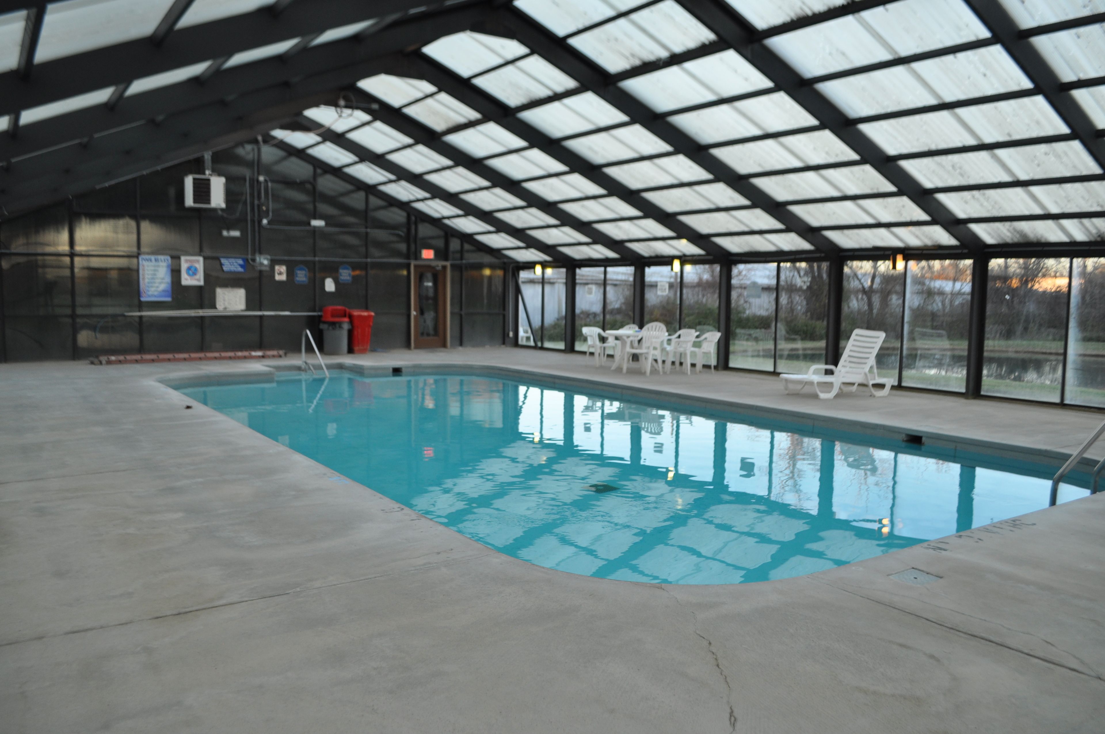 Une piscine intérieure dotée d’un toit en verre, de chaises longues blanches et d’une poubelle rouge.