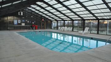 Une piscine intérieure dotée d’un toit en verre, de chaises longues blanches et d’une poubelle rouge.