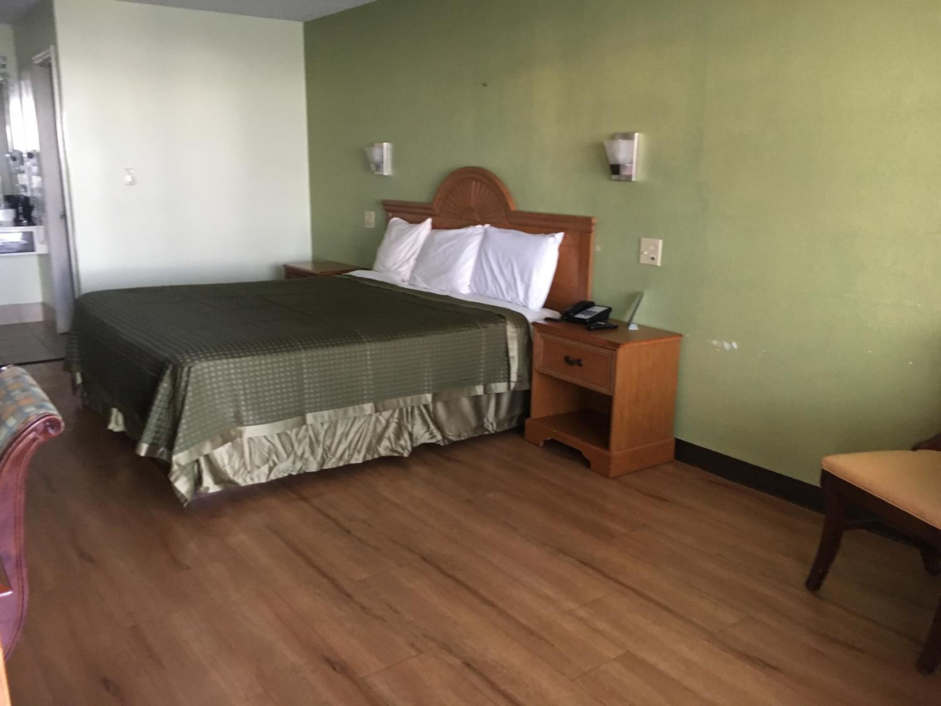 A hotel room with a bed, a nightstand with a phone, and a chair.