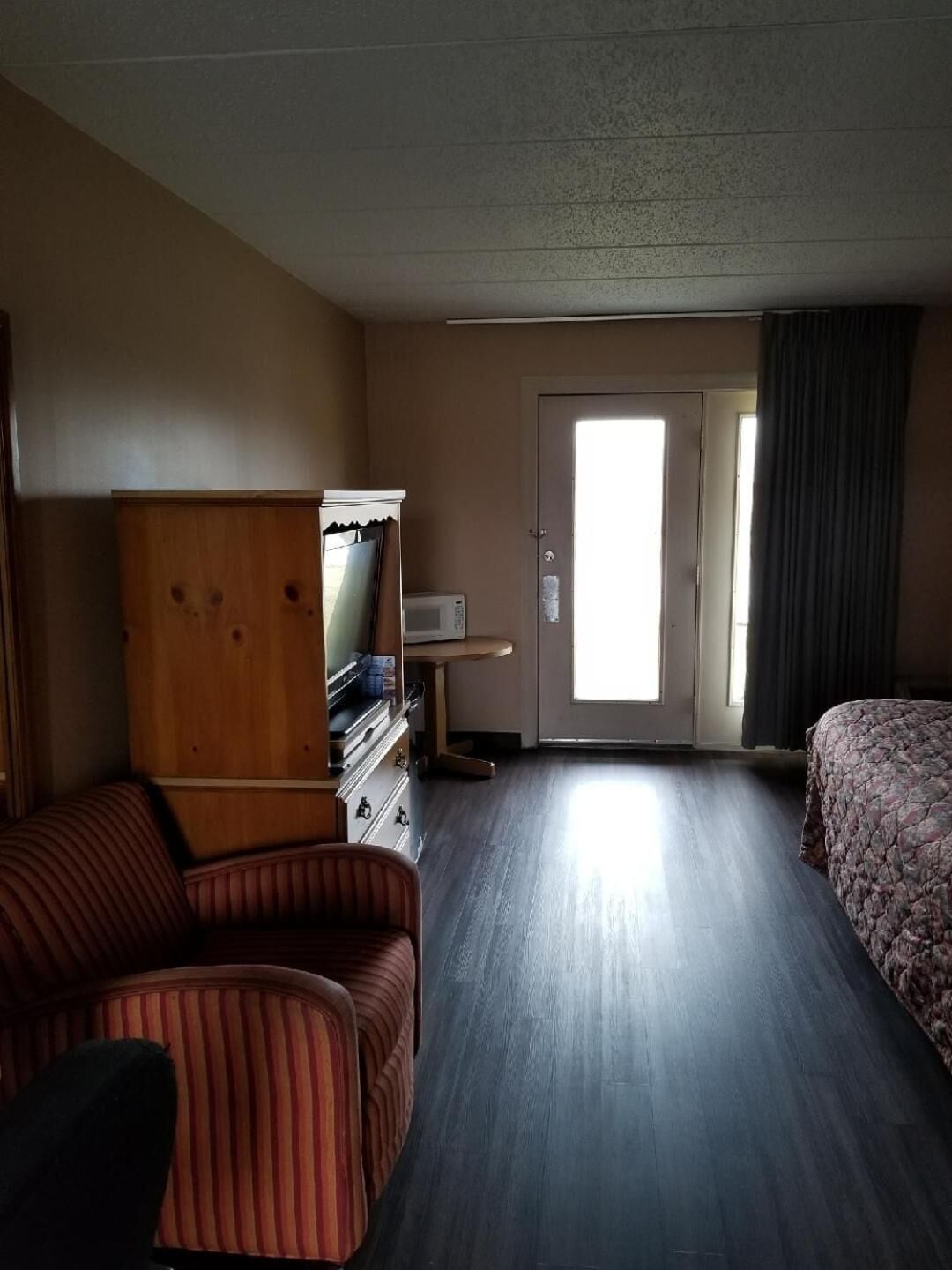 A hotel room with a wooden wardrobe, a television, a bed, and a sofa.