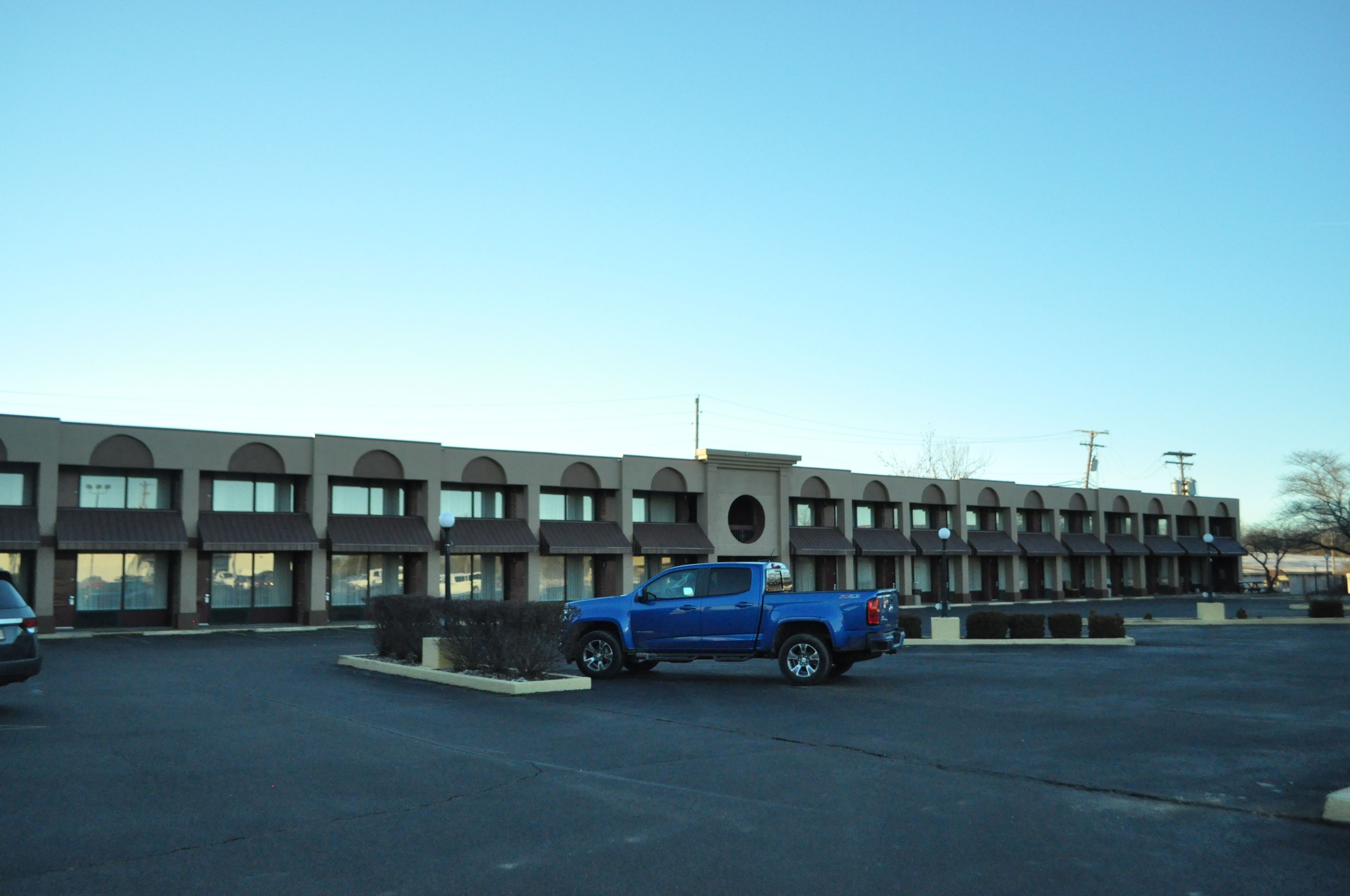 A motel with a row of rooms, a parking lot, and a blue truck parked in front.