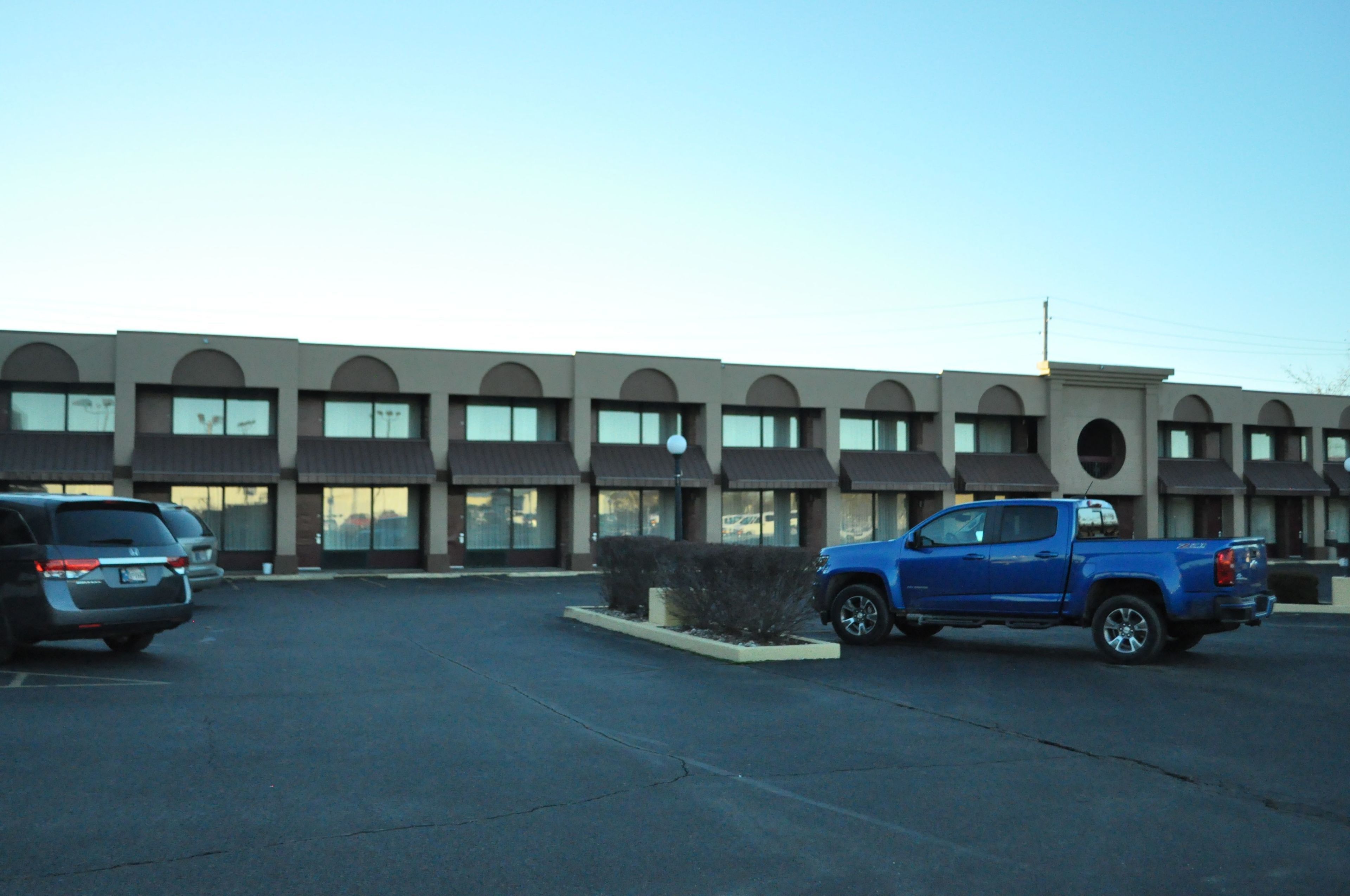 Un edificio con una hilera de ventanas y un estacionamiento con dos vehículos.