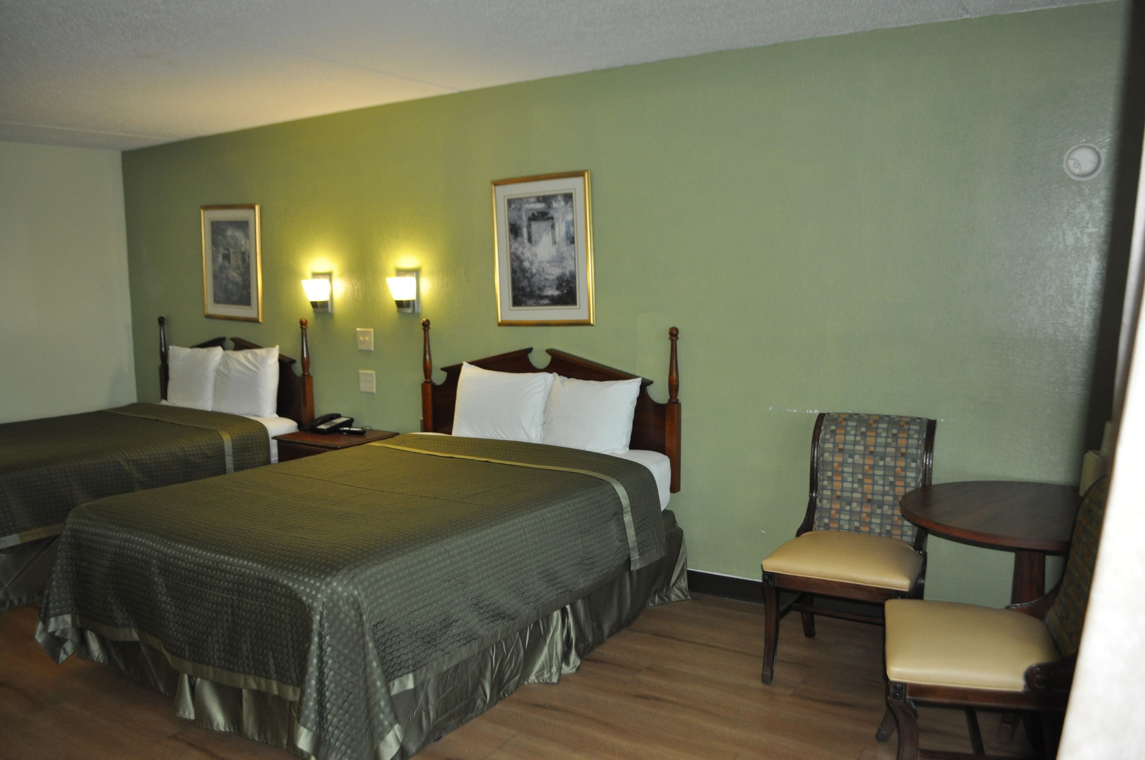 A hotel room with two single beds, a chair, a small table, and two wall-mounted lamps.