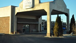 Ein West Way Inn mit Backsteinfassade, überdachtem Parkplatz und blauem Himmel.