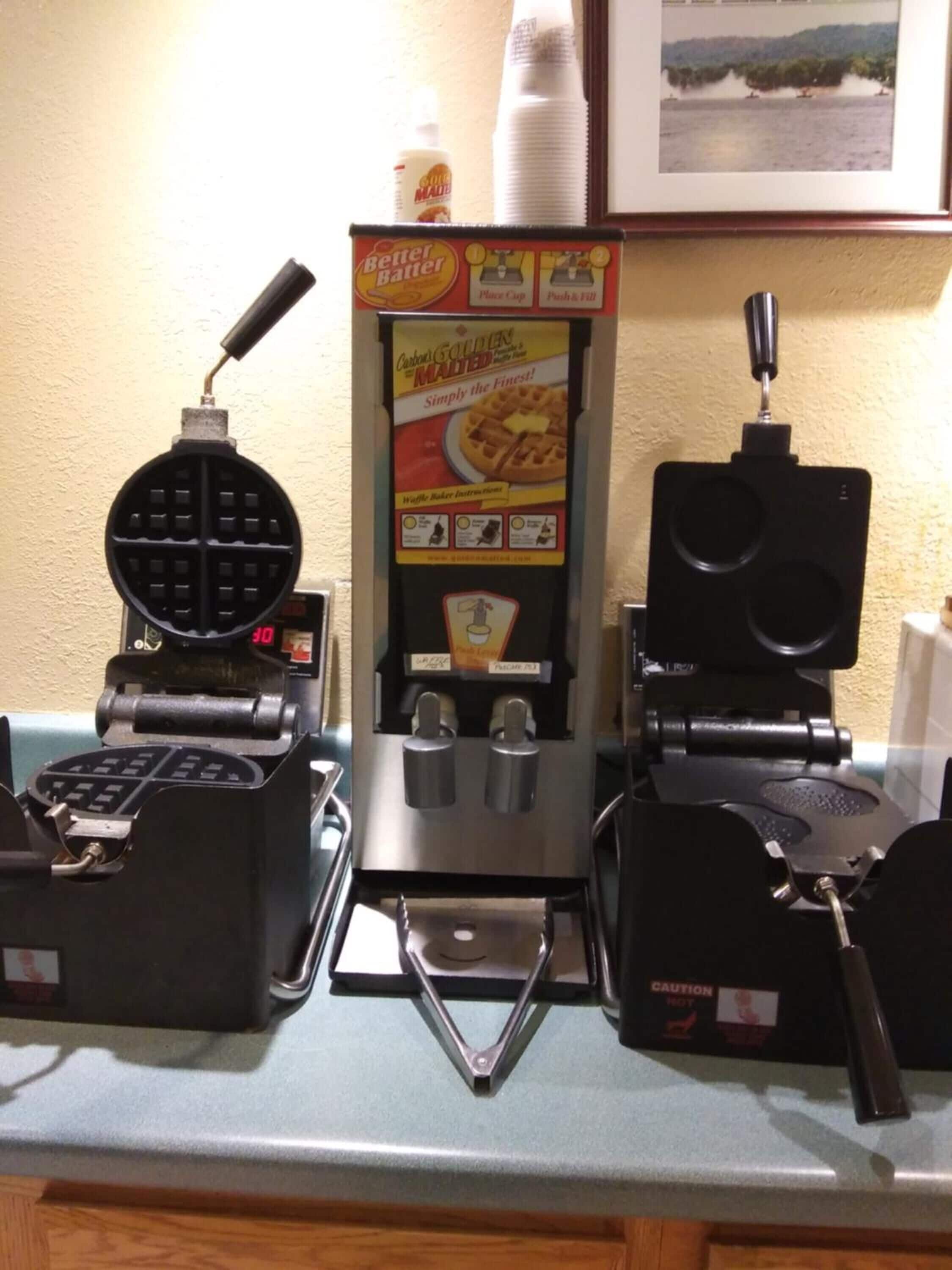 A waffle iron, a waffle maker, and a waffle maker box on a kitchen counter.