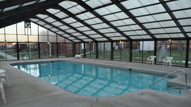 Ein Hallenbad mit Glasdach, Betonboden und weißen Stühlen rund um den Pool.