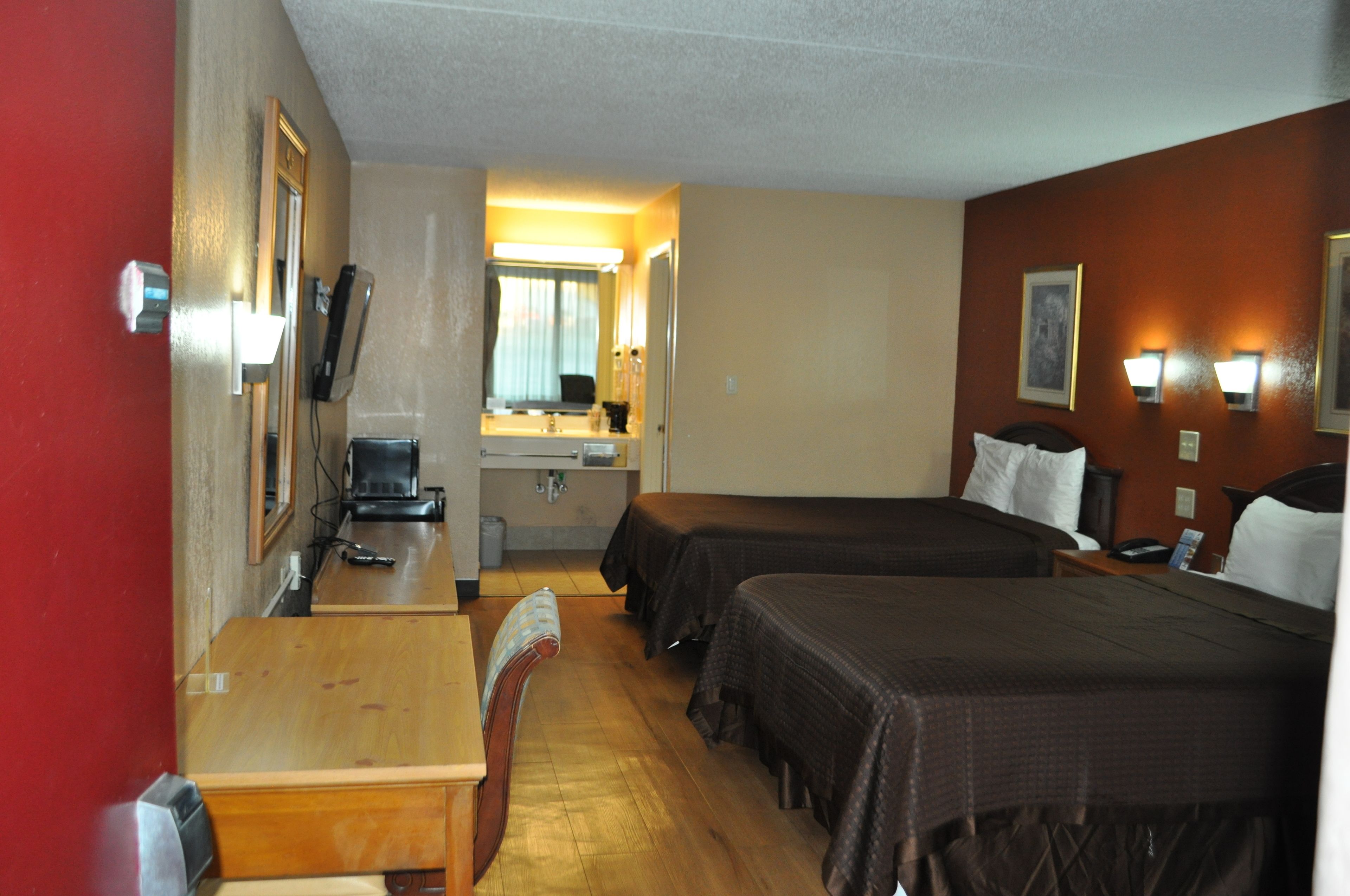 A hotel room with two beds, a desk, a chair, a mirror, a sink, and a telephone.