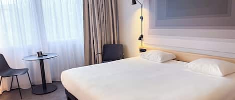 Una habitación de hotel con una cama grande, una mesita de noche, una silla, un escritorio y una lámpara.