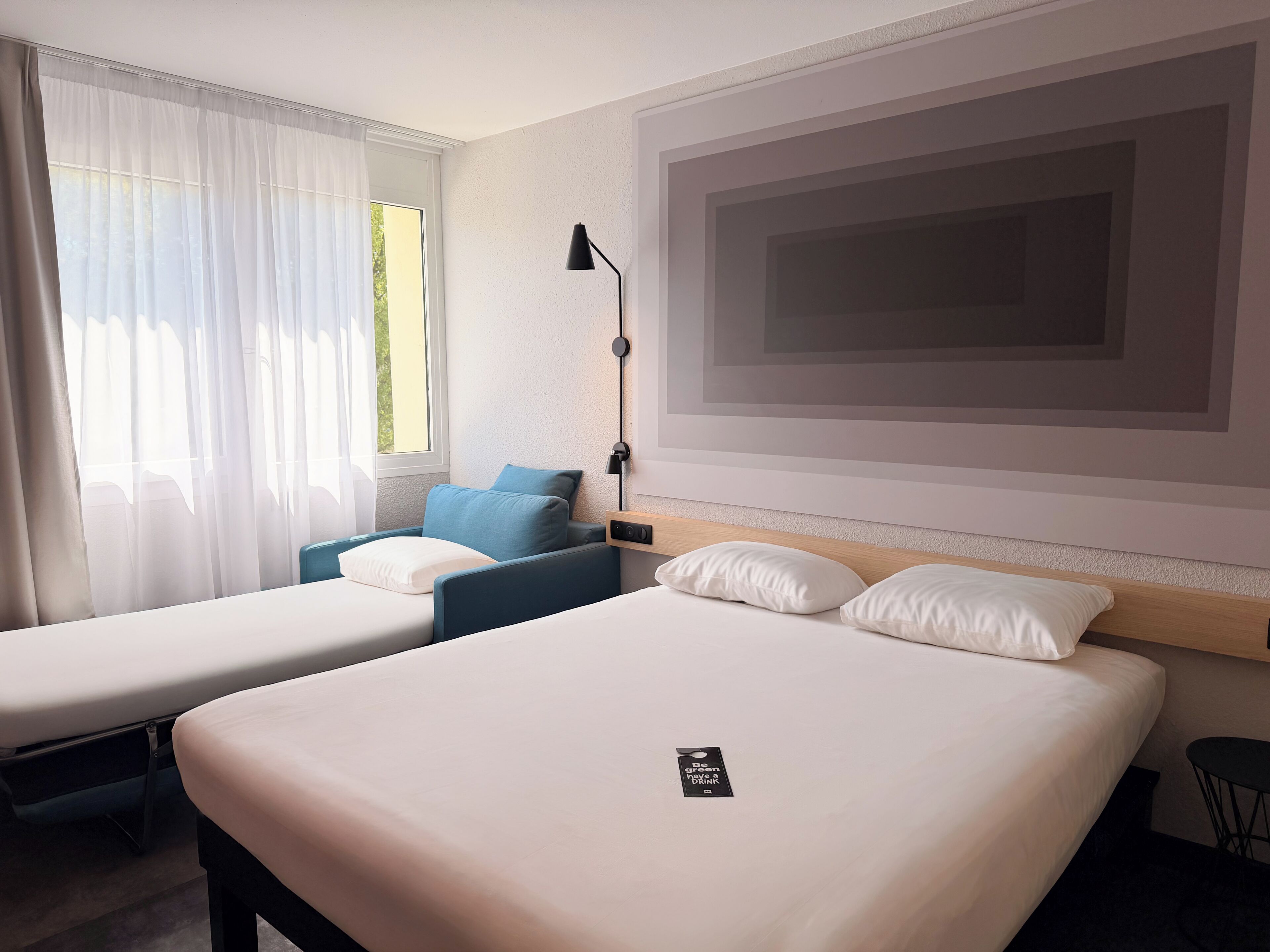 A hotel room with two beds, a desk, a chair, and a large window with curtains.