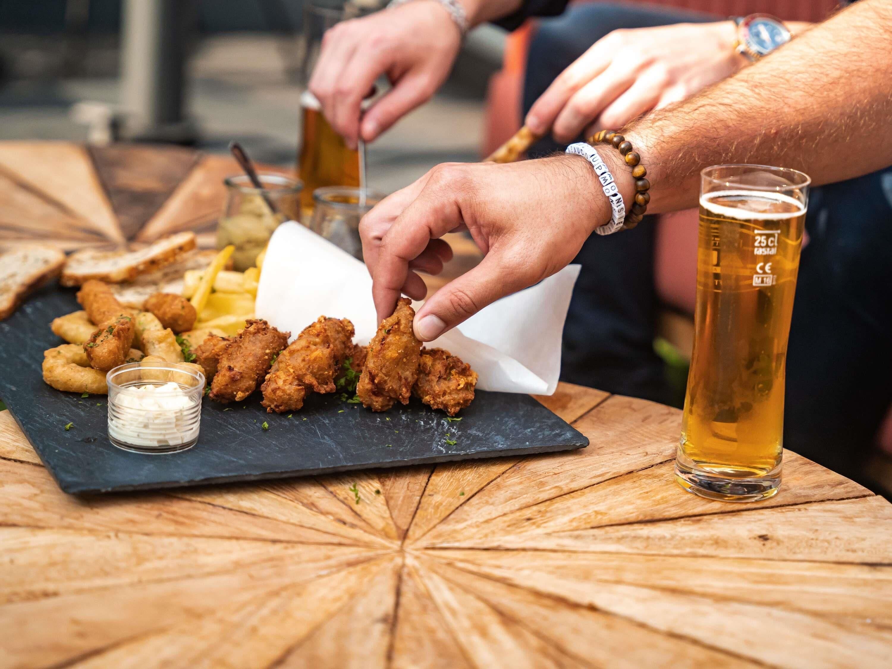 A meal with fried chicken, fries, and a small cup of sauce on a slate board.
