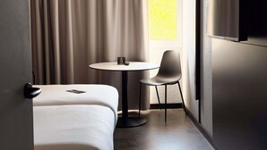 A hotel room with a bed, a round table with a chair, a TV mounted on the wall, and a window with curtains. - ibis Ales Centre Ville Hotel (Ales)