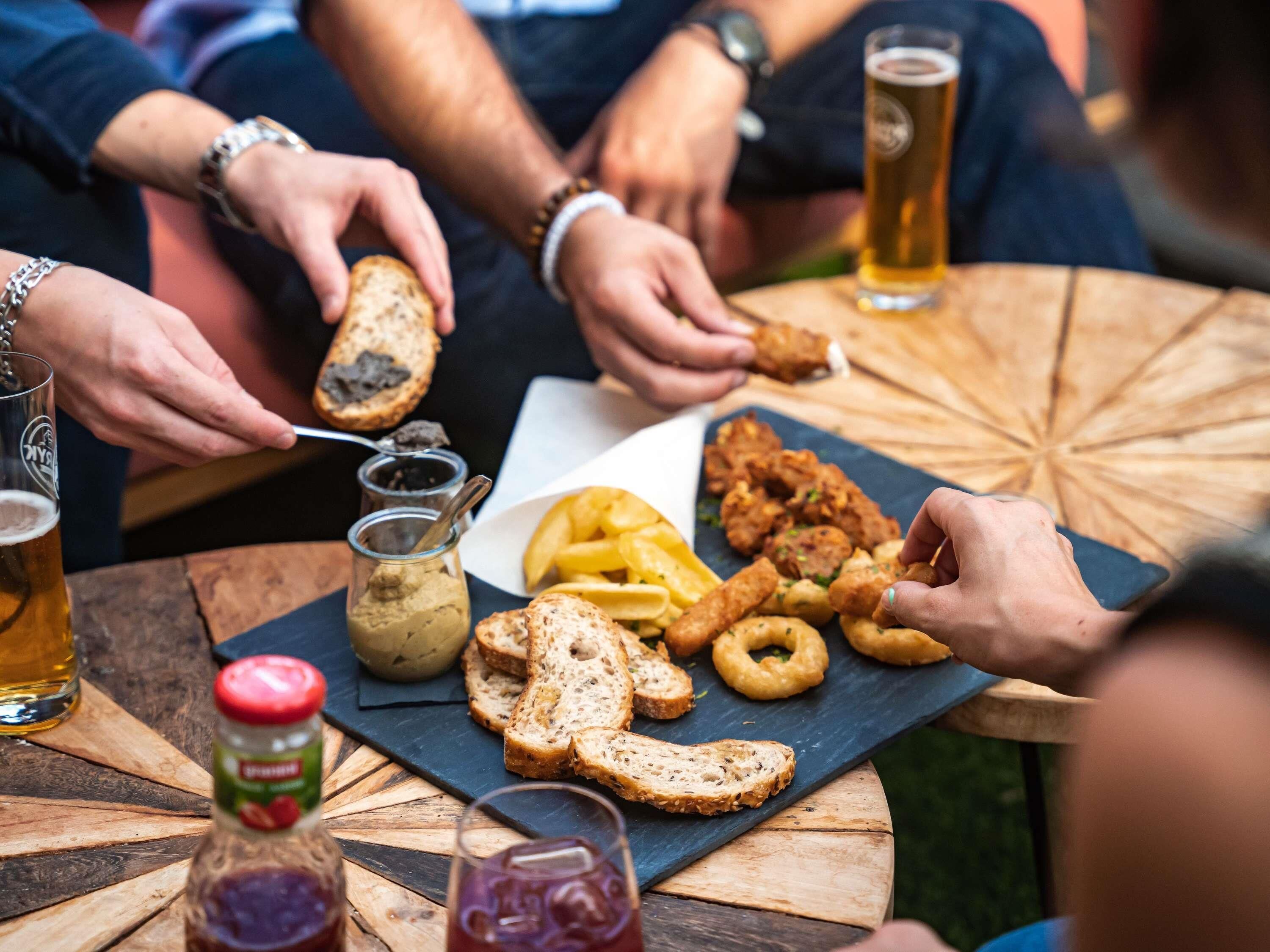 Een ronde houten tafel met diverse soorten eten en drinken, zoals brood, gefrituurde snacks en een fles saus.