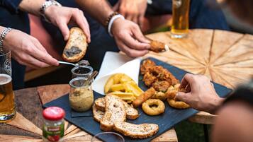Een ronde houten tafel met diverse soorten eten en drinken, zoals brood, gefrituurde snacks en een fles saus.
