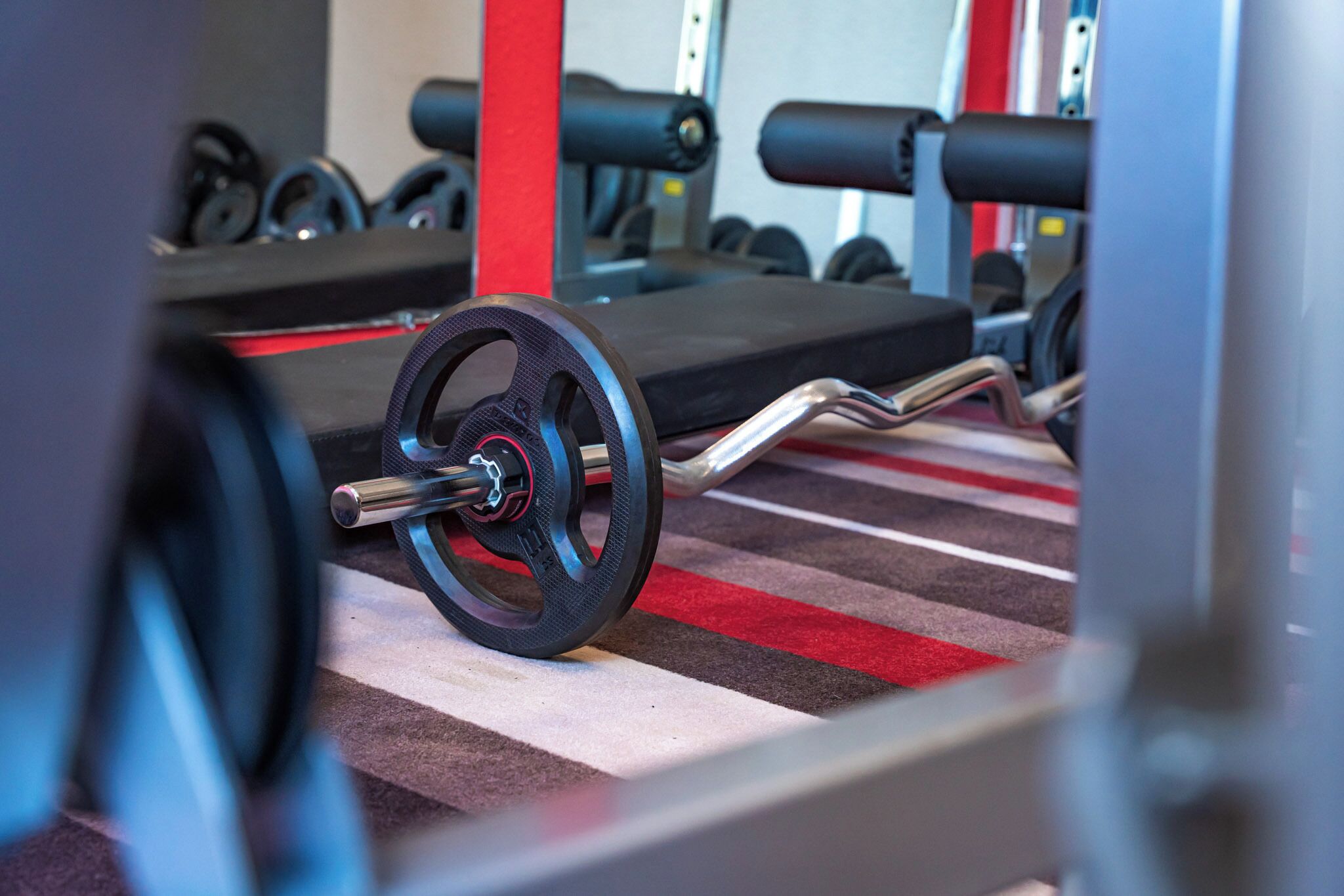 A gym with weightlifting equipment, including a barbell and weights, on a striped floor.