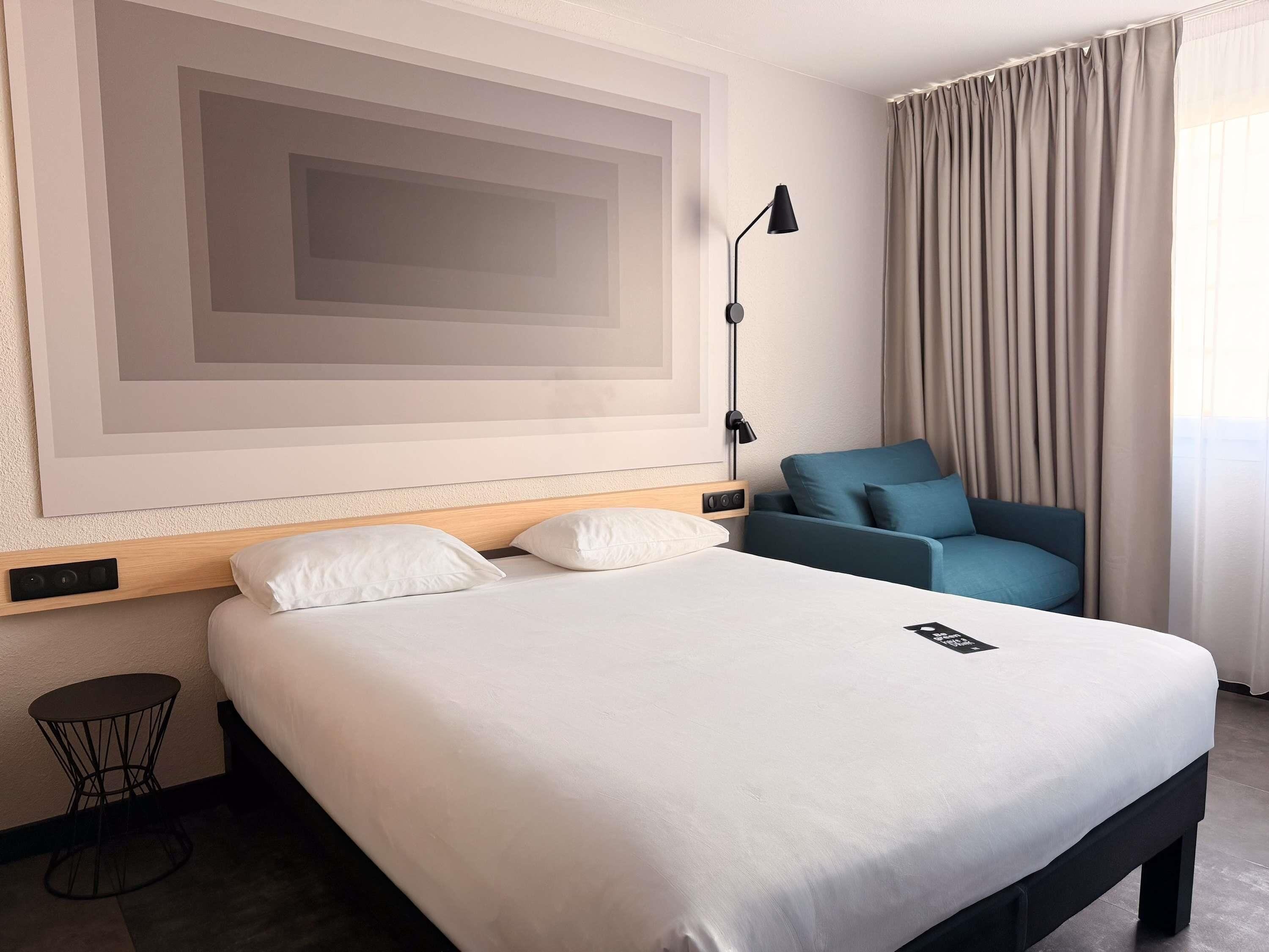 Habitación de hotel con una cama grande, un sofá, una lámpara y una obra de arte en la pared.