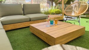 A wooden coffee table with a glass of blue liquid and a glass with a yellow liquid, a wicker chair, and a grey sofa in an outdoor setting. - ibis Ales Centre Ville Hotel (Ales)