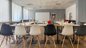 A conference room with a long table, chairs, a projector screen, and a whiteboard. - ibis Ales Centre Ville Hotel (Ales)