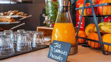 Dispensador de jugo con un cartel que indica 'Jus D'Orange Pressées' y una exhibición de frutas con naranjas y plátanos.