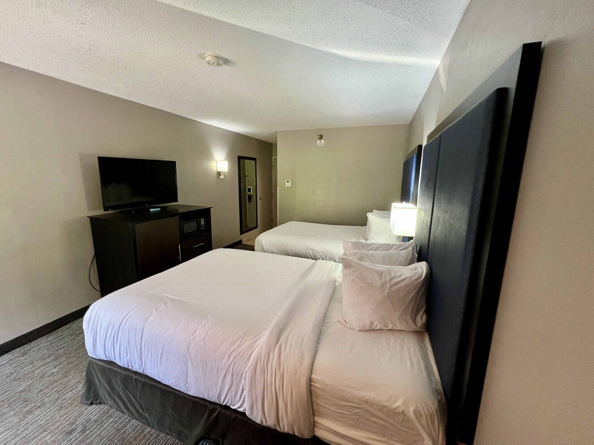 Habitación de hotel con dos camas, televisor, escritorio y espejo.