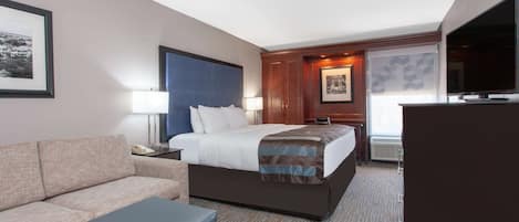 A hotel room with a bed, a sofa, a desk, a TV, and a framed picture on the wall.