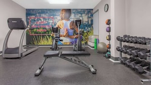 Ett gym med löpband, en motionscykel, en bänkpress och ett ställ med hantlar.